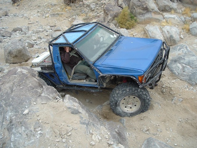 Blue caged 4x4 trail rig crawling over desert rocks with driver at the wheel