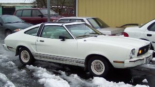 1978 Ford Mustang II - A white 1978 Ford Mustang II coupe is parked outdoors with snow on the ground, alongside other vehicles.