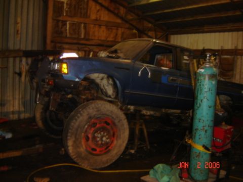1982 Nissan Titan - A blue pickup truck is elevated on stands inside a workshop, with welding equipment nearby.
