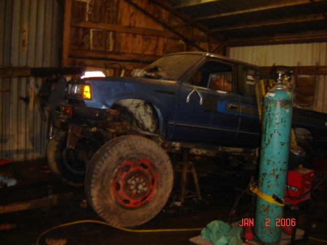 blue pickup truck on stands in a garage, looks like it's being worked on