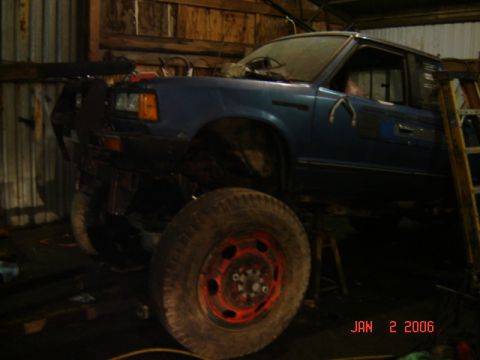 1982 Nissan Titan - A blue pickup truck with oversized wheels and a modified bumper is shown in a workshop.