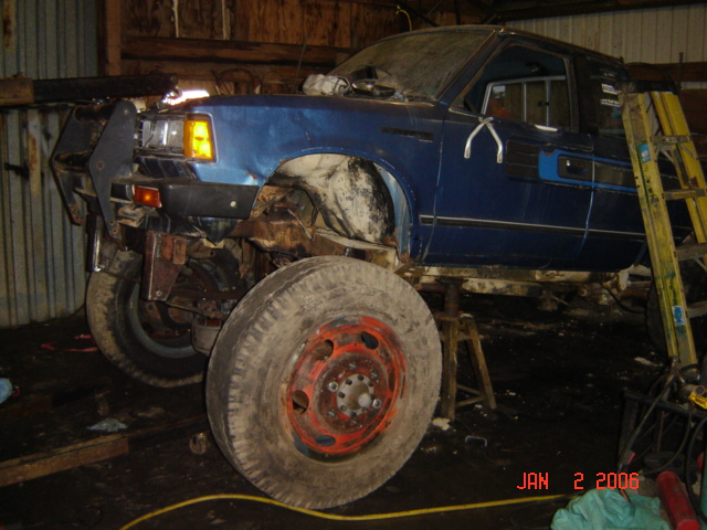 Blue pickup truck with large tires, lifted, in a garage