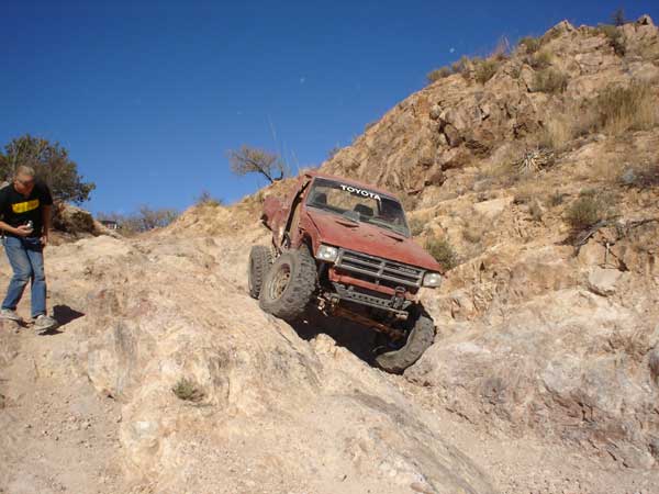 Red Toyota truck with off-road modifications climbing a steep, rocky incline under a clear blue sky