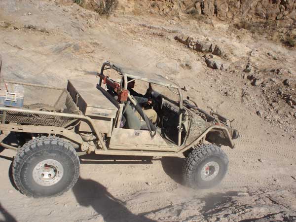 Off-road buggy with a bed and roll cage driving on a dirt hill