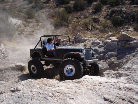 1989 Ford Bronco - This Jeep CJ-7 is navigating a challenging off-road course in a dusty, rocky environment.