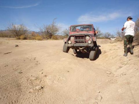 1989 Ford Bronco - A red jeep navigates a sandy incline under a clear blue sky.