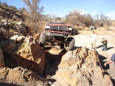 1989 Ford Bronco - This red Toyota truck navigates a rocky trail, with other vehicles and people in the background.