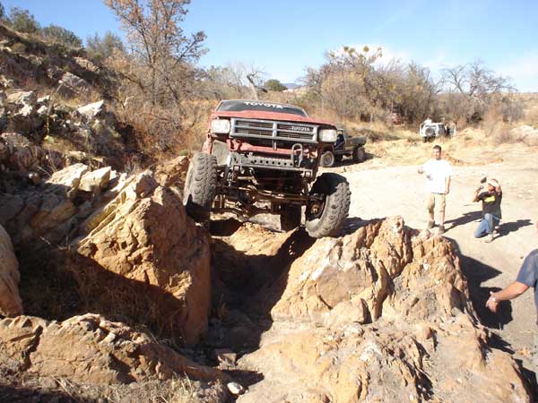 Red Toyota truck climbing rocks, front 3/4 view. Readable text on grille