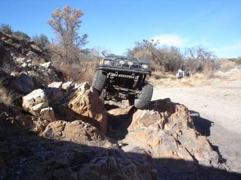 1989 Ford Bronco - 1989 Ford Bronco navigating a rocky off-road course under a clear blue sky.