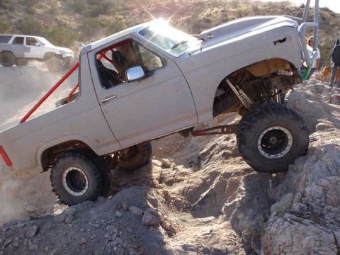 1989 Ford Bronco - Modified off-road truck navigates rocky terrain, with a white SUV visible on the trail behind it.