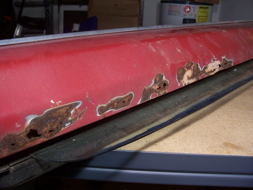 Red Bronco body panel on workbench with heavy rust holes along its lower edge