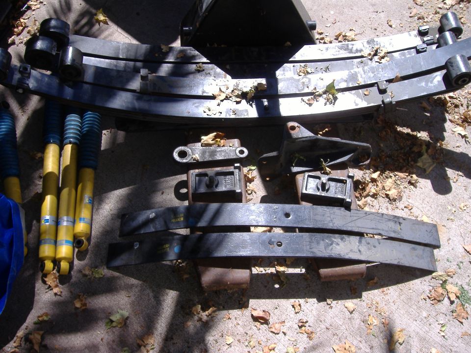 Lift kit parts including leaf springs, Bilstein shocks, and lift blocks laid out on a driveway
