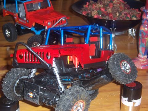 1999 Jeep TJ - Two red toy Jeeps are on a table, one in the foreground with a blue roll cage and the other in the background.
