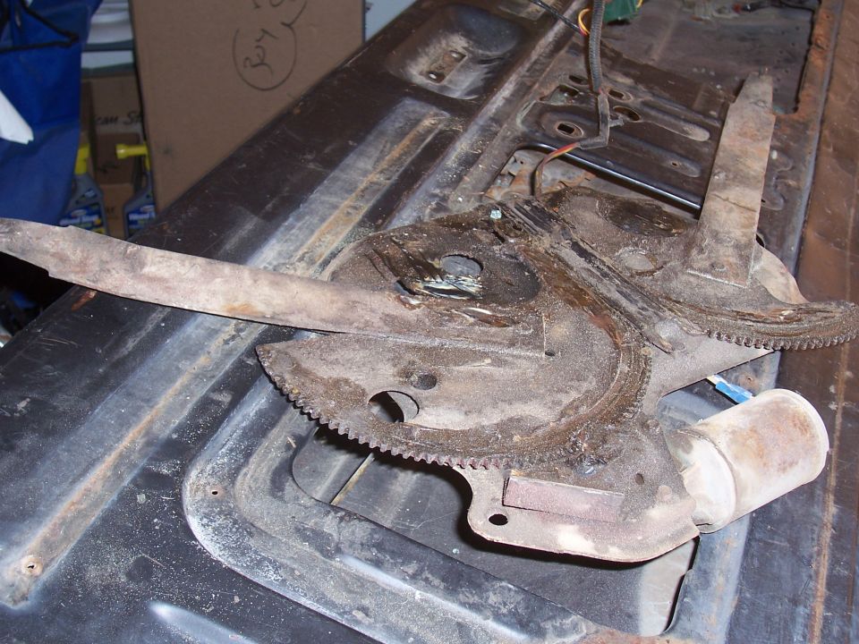 Dirty power window regulator with sector gears and motor removed, resting on a tailgate panel
