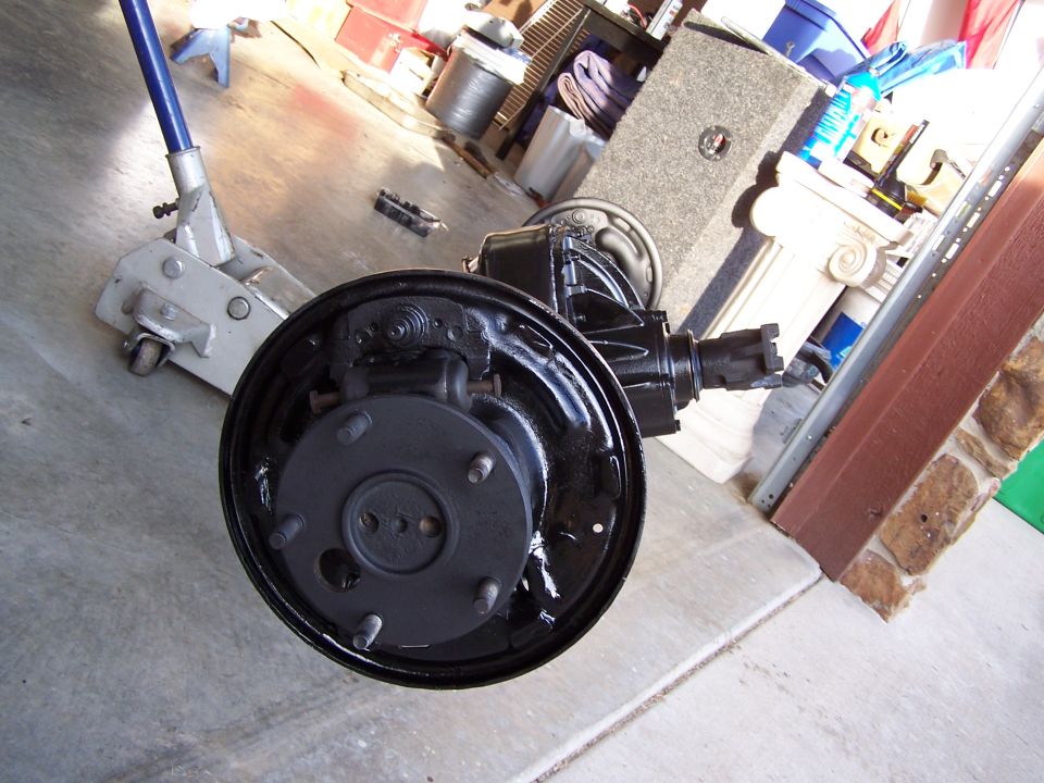 Rear axle assembly with drum brake and brake shoes, resting on a concrete floor next to a floor jack