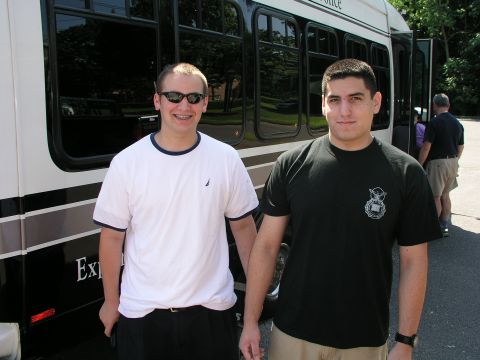 1999 Ford Crown Victoria - Two men pose in front of a bus with 'Police' visible on the side.