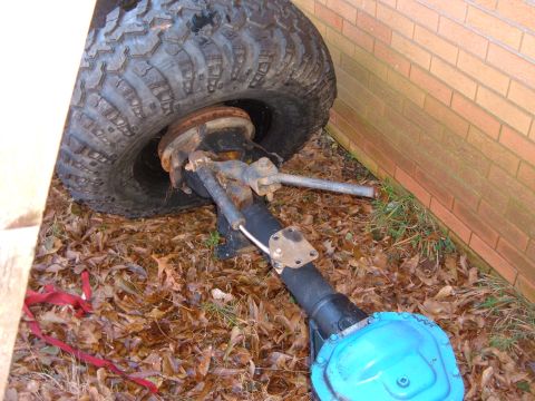1987 Ford Bronco - Close-up of a vehicle's front axle and tire assembly, resting on the ground.