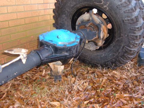 1987 Ford Bronco - Close-up of a vehicle axle with a blue differential cover and a large tire, set against a brick wall.