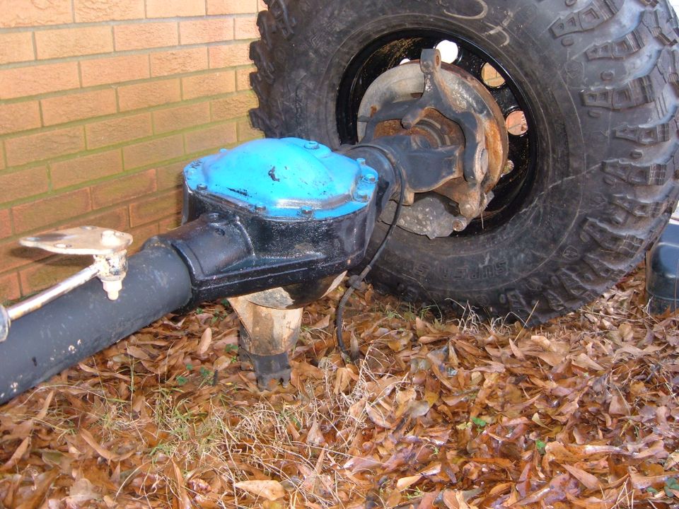 Axle assembly with blue differential cover and large tire, resting on dry leaves