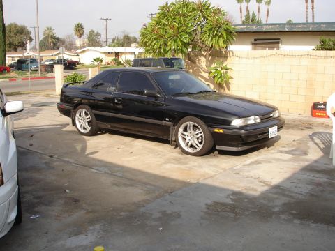 1989 Mazda MX-6 - A black 1989 Mazda MX-6 GT coupe is parked in a driveway, showing its distinctive body style and GT badging.
