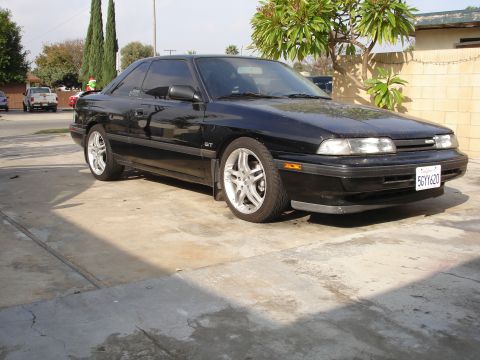 1989 Mazda MX-6 - A black 1989 Mazda MX-6 GT coupe is shown from the front 3/4 angle in a driveway.