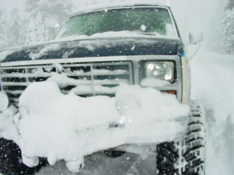 1986 Ford Bronco - A 1986 Ford Bronco is buried in snow, with only its front grille and headlights visible.