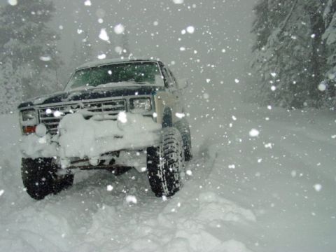 1986 Ford Bronco - 1986 Ford Bronco navigates a snowy road with trees in the background.