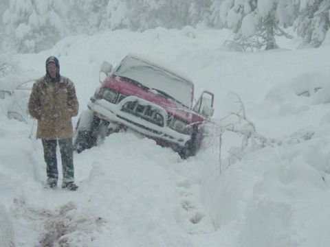 1986 Ford Bronco - A person stands beside a red SUV that is buried in snow, indicating difficult driving conditions.
