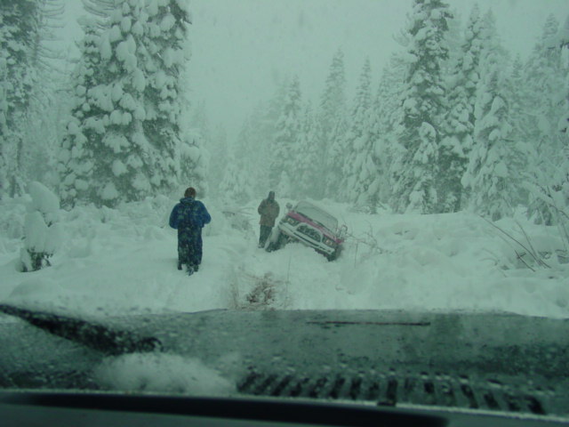 Red SUV stuck in deep snow, front grille visible, two people standing nearby
