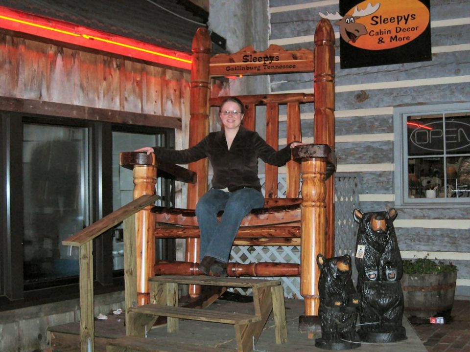 Giant wooden rocking chair with a woman sitting in it, outside a shop with bear statues
