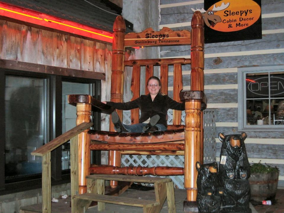 Person sitting in a giant wooden chair outside Sleepy's in Gatlinburg, Tennessee. Bear carvings are nearby
