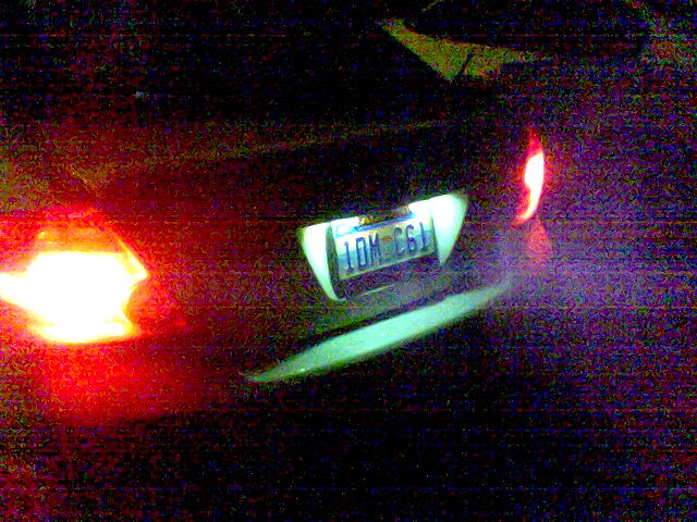 Grainy night rear view of a car with glowing red taillights and lit license plate