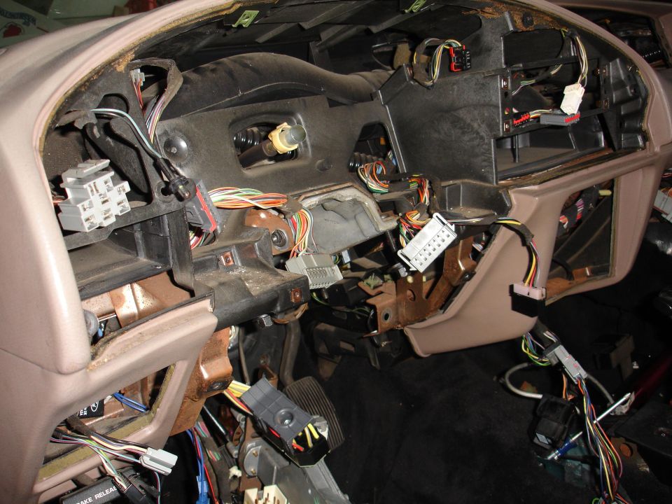 Car dashboard with many wires and connectors exposed, looks like it's being worked on