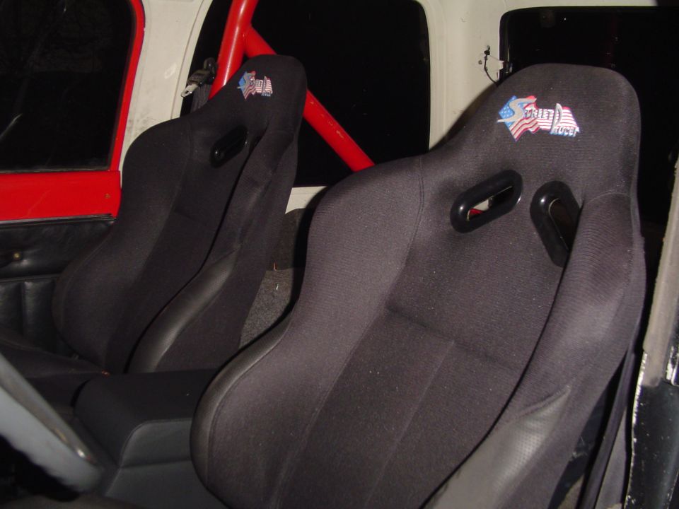 Two black racing seats with an American flag logo on the headrests, inside a vehicle with a red roll cage