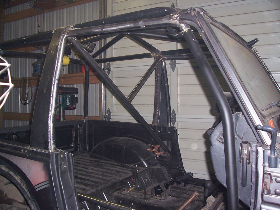 Tube roll cage fabricated inside a stripped truck cab in a metal-walled shop