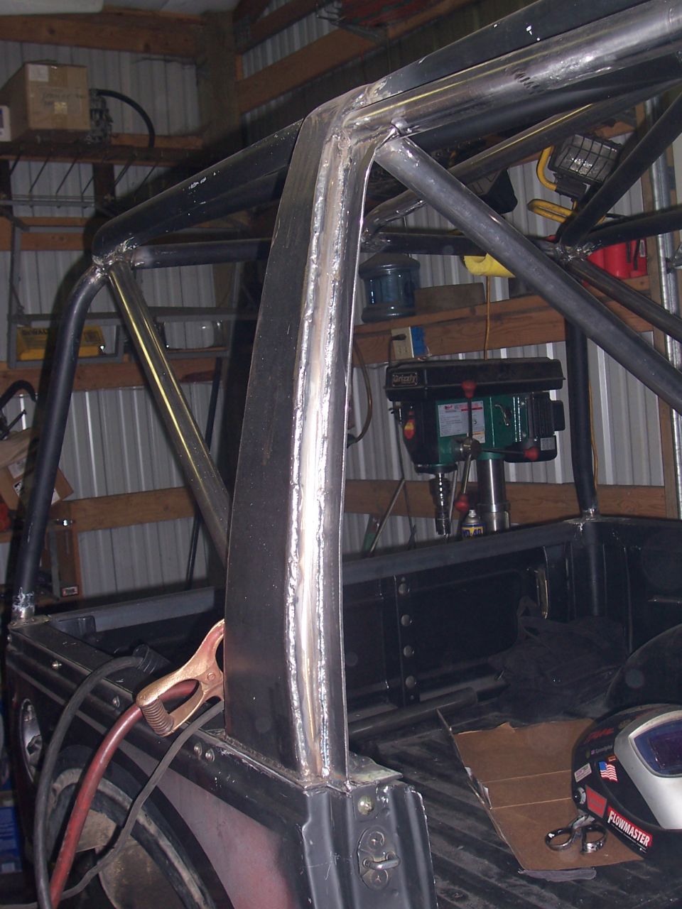Welding a custom roll cage inside a vehicle, with a drill press in the background