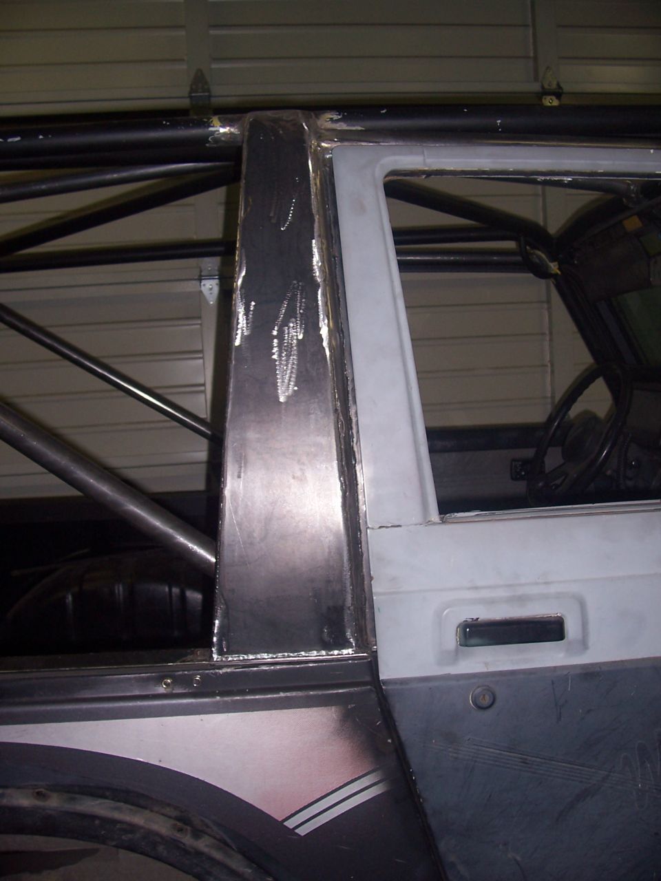 Vehicle interior with roll cage, custom metalwork on A-pillar, and door handle