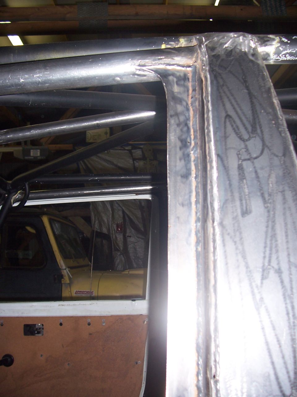 Roll cage structure inside a vehicle with a brown door panel and a glimpse of a yellow vehicle through the window
