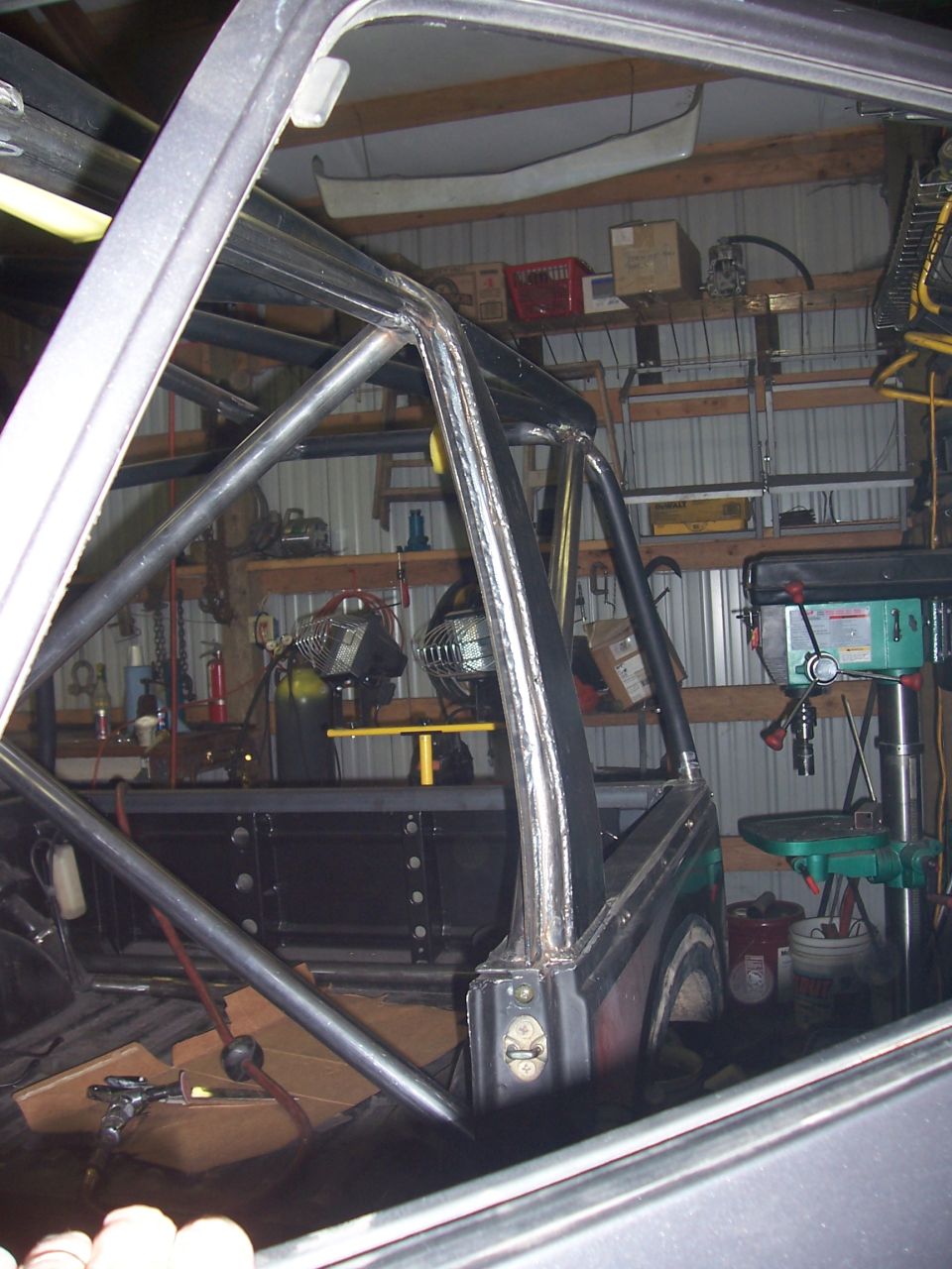 Interior view of a vehicle with a custom roll cage being installed, showing metal tubing and welding work