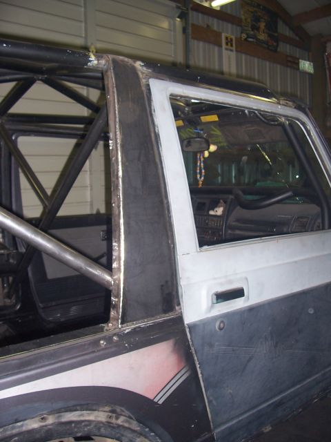 1988 Suzuki Samurai - The interior of a modified Suzuki Samurai shows a custom roll cage and a partially disassembled door panel.