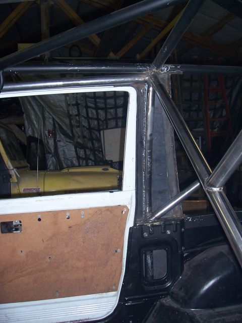 1988 Suzuki Samurai - The interior of a vehicle shows a custom roll cage installation and a partially stripped door panel.