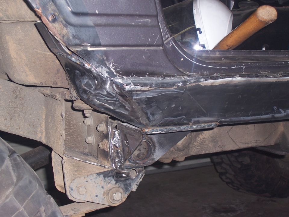 Close-up of a heavily modified vehicle frame and body section with visible welding and rust