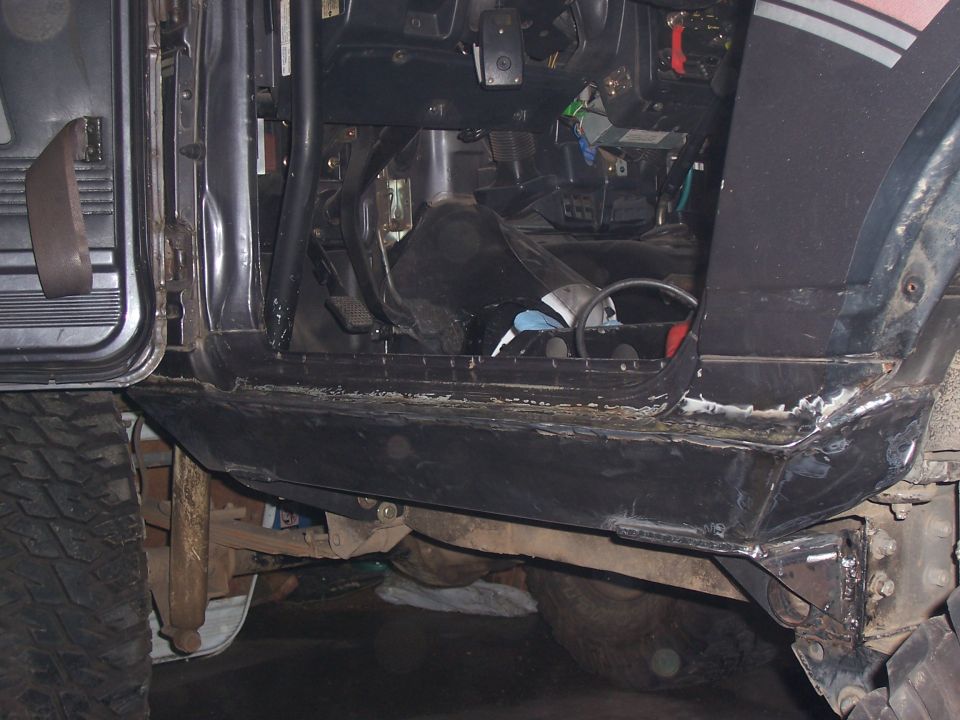 Off-road vehicle interior showing pedals, steering wheel, and door panel. Rocker panel area is modified