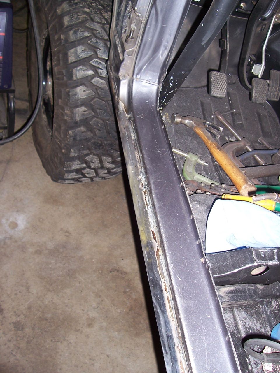 Gray vehicle interior with tools, large off-road tire, and rusty door sill