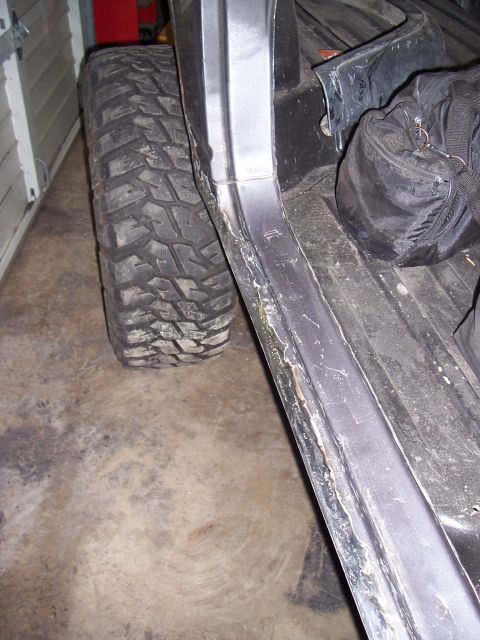 1988 Suzuki Samurai - Close-up view of a large off-road tire and the side of a vehicle's body, showing wear and tear.