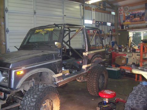 1988 Suzuki Samurai - A dark Suzuki Samurai with a roll cage and "Trail Tough" sticker is parked inside a garage.