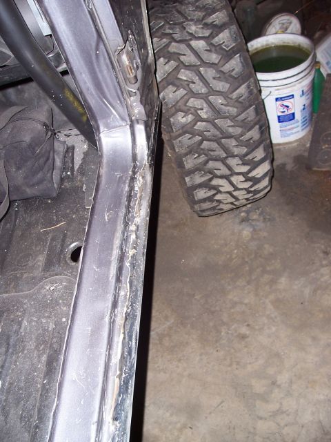 1988 Suzuki Samurai - Close-up of an off-road tire positioned next to the interior of a vehicle, showing a roll cage and door frame.
