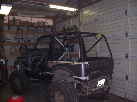 1988 Suzuki Samurai - A modified Suzuki Samurai with a custom roll cage is parked inside a garage, showing its lifted suspension and off-road tires.