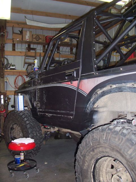 1988 Suzuki Samurai - A black 1988 Suzuki Samurai with a custom roll cage and large tires is parked in a garage.