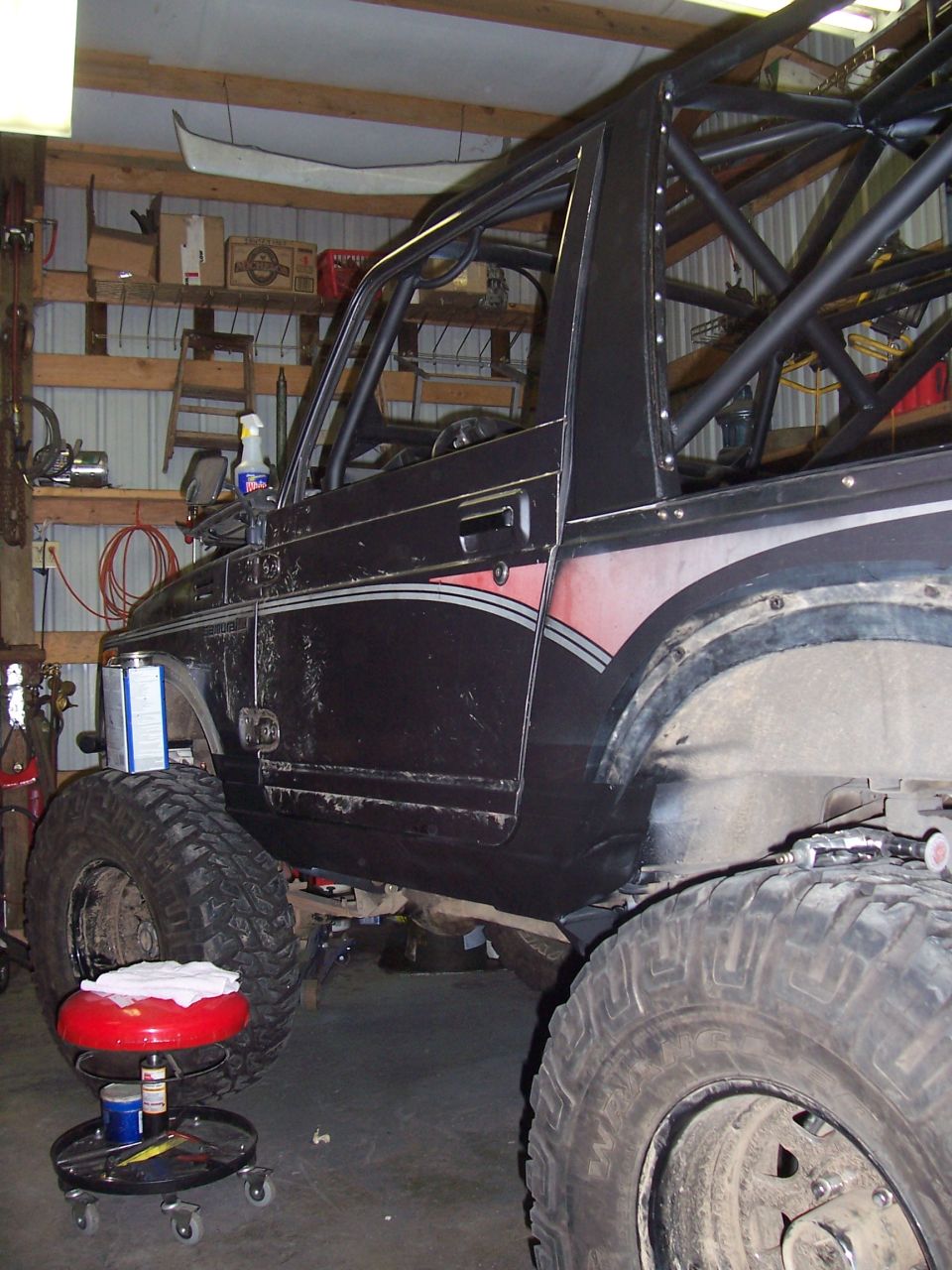 Black 1988 Suzuki Samurai with roll cage, lifted, large tires, in a garage